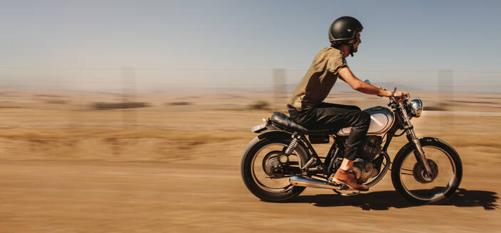 Seitenansicht eines jungen Mannes, der auf einer Landstraße Motorrad fährt. Männlicher Fahrer, der auf einem Feldweg auf dem Land Motorrad fährt. - JLPSF22132