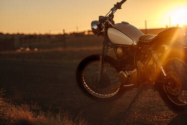 Klassisches Motorrad, das während des Sonnenuntergangs auf der Straße steht. Oldtimer-Motorradpark auf der Seite der Landstraße. - JLPSF22149