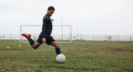 Fußballspieler auf dem Feld, der den Ball kickt. Ein Mann spielt Fußball auf einem Feld an einem bewölkten Morgen. - JLPSF22152