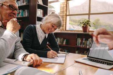 Ältere Frau, die mit ihren männlichen Kollegen in einer Bibliothek sitzt und Notizen schreibt. Ältere Menschen, die in einem Universitätskollegium diskutieren und lernen. - JLPSF22154