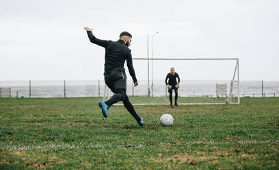 Fußballer, der einen Strafstoß schießt. Fußballspieler, der den Ball in Richtung Torpfosten schießt, während der Torwart in Position ist. - JLPSF22170