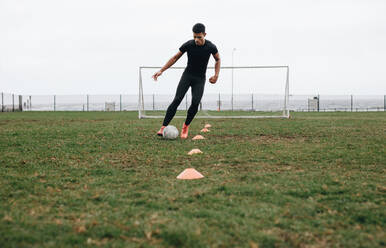 Fußballer bei einer Dribbelübung auf dem Feld. Fußballer bewegt den Ball zwischen den Kegeln und übt das Dribbeln. - JLPSF22174