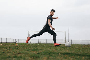 Fußballspieler in der Position, einen Fußball zu kicken. Fußballer übt sein Spiel auf dem Feld früh am Morgen. - JLPSF22175