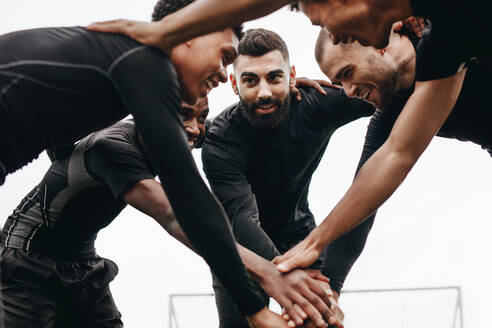 Low angle view of footballers talking about the game plan standing in a huddle. Soccer players holding their hands standing in a huddle and cheering themselves up. - JLPSF22178