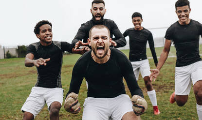 Der Torwart macht vor Aufregung eine Grätsche, nachdem er das Spiel gewonnen hat. Fußballkollegen feiern den Erfolg mit Freudenschreien auf dem Spielfeld. - JLPSF22185