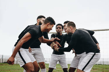 Fußballspieler, die sich an den Händen halten und sich gegenseitig aufmuntern. Fußballer, die in der Nähe des Torpfostens stehen und sich gegenseitig aufmuntern. - JLPSF22194