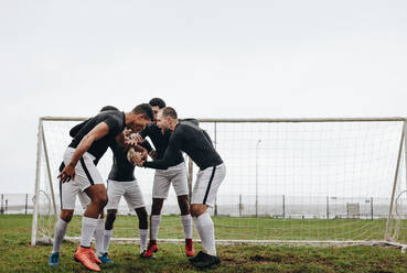 Fußballspieler, die sich an den Händen fassen, in einem Huddle stehen und aufmunternde Worte sprechen. Fußballer, die sich in einem Huddle auf dem Spielfeld aufmuntern. - JLPSF22195