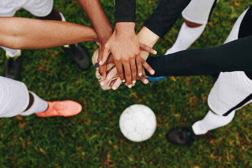 Draufsicht auf die Hände von Spielern, die übereinander in einem Huddle stehen. Spieler, die in einem Huddle stehen und ihre Hände in der Mitte mit einem Fußball auf dem Boden vereinen. - JLPSF22197