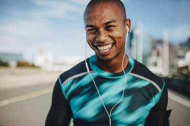 Fit young male runner with a broad smile. Young man in sports shirt and earphones looking at camera. - JLPSF22214