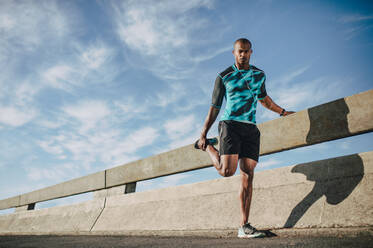 Afroamerikanischer Mann in Sportkleidung steht an der Straße und streckt die Beine. Sportler wärmt sich vor einem Lauf am Morgen in der Stadt auf. - JLPSF22216