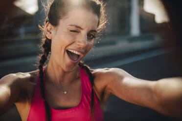 Läuferin, die morgens im Freien steht und in die Kamera zwinkert. Fitness-Frau, die während einer Trainingspause Spaß hat. - JLPSF22223