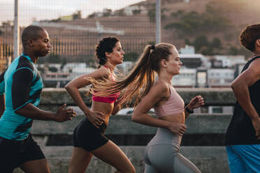 Eine Gruppe von Läufern in Fitnesskleidung läuft in der Stadt. Junge Männer und Frauen laufen am Morgen zusammen. - JLPSF22229