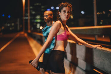 Fit junge Frau tun Stretching Training mit männlichen Freund im Freien auf der Straße der Stadt in der Nacht. - JLPSF22240