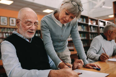 Senior woman lecturer guiding a senior man at college. Senior man sitting in class with his lecturer guiding him in learning. - JLPSF22256