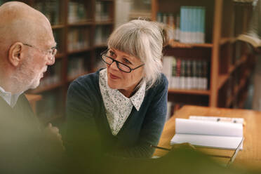 Älterer Mann und Frau diskutieren in einem Klassenzimmer einer Universität. Nahaufnahme eines älteren Paares, das in einer Bibliothek sitzt und mit Büchern auf dem Tisch diskutiert. - JLPSF22264