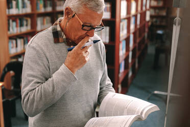 Universitätsprofessor, der in einer Klasse unterrichtet, stehend mit einem Buch und einem Marker in der Hand. Älterer Mann, der in einem Klassenzimmer stehend ein Buch mit Konzentration liest. - JLPSF22273