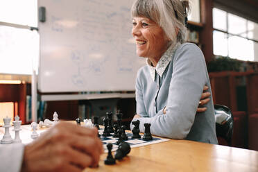 Nahaufnahme einer älteren Frau, die im Klassenzimmer sitzt und mit einem Kollegen Schach spielt. Fröhliche ältere Frau, die sich an einer Schachpartie erfreut. - JLPSF22289