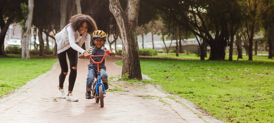 Kleiner Vorschuljunge und seine Mutter im Park mit einem Fahrrad. Mutter bringt ihrem Sohn das Radfahren im Park bei. - JLPSF22299