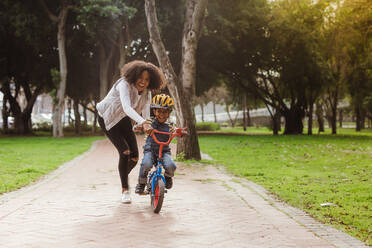 Cute boy learning to ride a bicycle with his mother. Woman teaching son to ride bicycle at park. - JLPSF22300