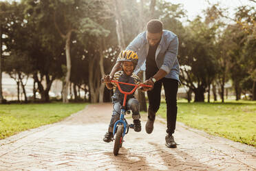 Junge lernt mit seinem Vater im Park Fahrrad fahren. Vater bringt seinem Sohn im Park das Radfahren bei. - JLPSF22304