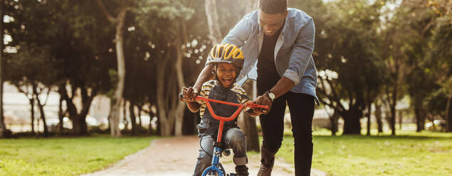 Junge lernt mit seinem Vater im Park Fahrrad fahren. Vater bringt seinem Sohn im Park das Radfahren bei. - JLPSF22305