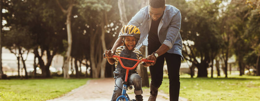 Boy learning to ride a bicycle with his father in park. Father teaching his son cycling at park. - JLPSF22305