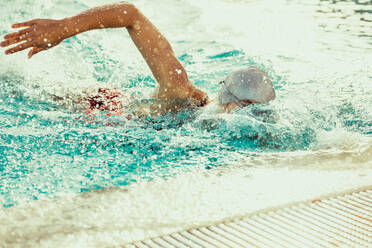 Female athlete swimmer swimming freestyle in pool. Woman practising swimming in pool. - JLPSF22375