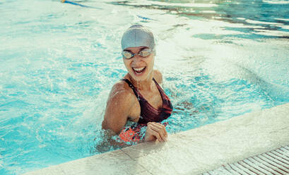 Fröhliche junge Frau in Badekleidung lachend am Beckenrand. Lächelnde Profischwimmerin im Pool. - JLPSF22376