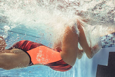 Aufnahme einer professionellen Schwimmerin in Aktion im Schwimmbecken. Junge Frau dreht sich beim Schwimmen vom Beckenrand aus unter Wasser um. - JLPSF22390