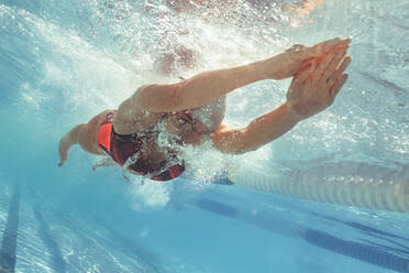 Unterwasseraufnahme einer Schwimmerin, die im Schwimmbecken gleitet, mit den Armen nach vorne gestreckt, mit dem Kopf zwischen den Armen und den Füßen auf dem Rücken - JLPSF22395