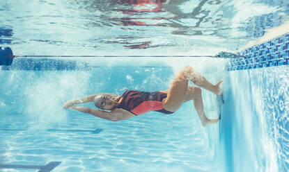 Aufnahme einer professionellen Schwimmerin, die sich beim Schwimmen unter Wasser umdreht. Eine Schwimmerin in Aktion im Schwimmbad. - JLPSF22397