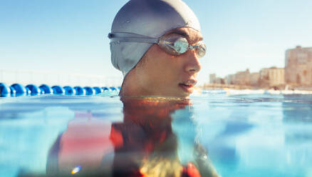 Nahaufnahme des Gesichts einer Schwimmerin außerhalb des Wassers. Eine Sportlerin trägt eine Badekappe und eine Schwimmbrille im Schwimmbad. - JLPSF22399