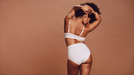 Smiling young woman wearing beige underwear in a studio. Body positive young  woman standing sideways against a studio background. Confident young woman  embracing her natural body and curves. stock photo