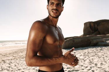 Ein Mann entspannt sich beim Fitnesstraining am Strand. Ein athletischer Mann mit nacktem Oberkörper steht am Strand und schaut weg. - JLPSF22522