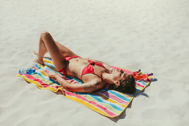 Frau im Badeanzug auf einem Handtuch liegend beim Sonnenbaden am Strand. Frau im Urlaub beim Entspannen am Strand an einem sonnigen Tag. - JLPSF22539