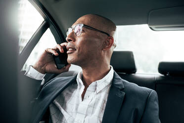 Businessman wearing eyeglasses talking over cell phone sitting in his sedan looking out the window. Man managing business on mobile phone sitting in car. - JLPSF22600