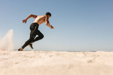 Mann beim Fitnesstraining am Strand an einem sonnigen Tag. Seitenansicht eines sportlichen Mannes beim Laufen am Strand. - JLPSF22641