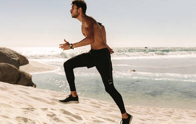 Mann beim Fitnesstraining am Strand an einem sonnigen Tag. Seitenansicht eines sportlichen Mannes beim Laufen am Strand. - JLPSF22645