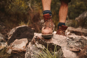 Nahaufnahme der Schuhe eines männlichen Wanderers auf einem felsigen Pfad, der in Trekkingstiefeln über einen unwegsamen Weg läuft. - JLPSF22651