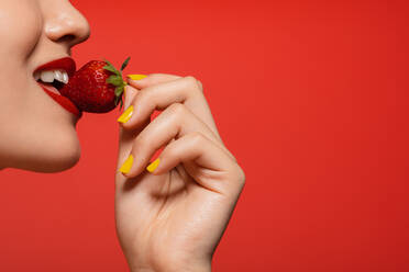 Studioaufnahme einer schönen jungen Frau, die eine Erdbeere vor rotem Hintergrund isst. Frau beißt in eine Erdbeere. - JLPSF22683