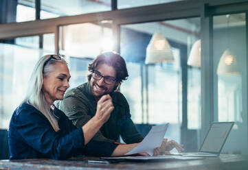 Business people meeting in office and discussing over a documents. Business woman with a financial report in hand sitting with male colleague looking at her and smiling. - JLPSF22715