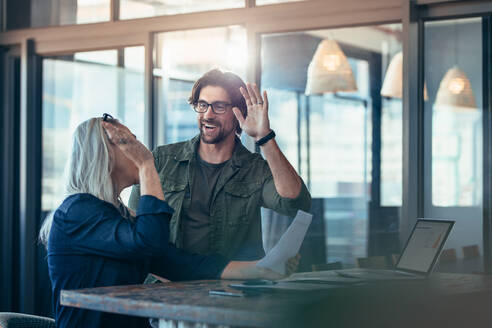 Two business colleagues giving each other a high five and smiling. Business team rejoicing success. - JLPSF22717