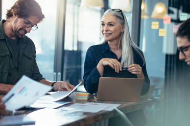 Team of professionals reviewing few finance documents in a meeting. Business team analyzing financials documents in a meeting. - JLPSF22737