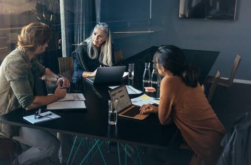 Three professionals sitting around a table and discussing work. Business team brainstorming new business ideas during meeting at office. - JLPSF22743