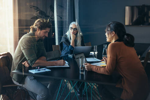 Business team sitting inside a meeting room and discussing work. Professionals sitting around a table brainstorming ideas. - JLPSF22744