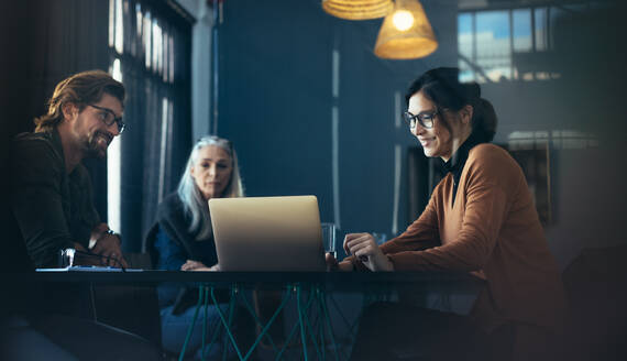 Geschäftsleute sitzen am Tisch und schauen auf den Laptop. Asiatische weibliche Führungskraft gibt eine Präsentation über Laptop an Kollegen im Büro. - JLPSF22747