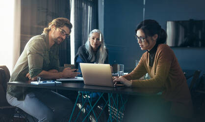 Drei Geschäftskollegen treffen sich in einem modernen Büro. Eine Geschäftsfrau zeigt ihrem Team einen Geschäftsplan auf einem Laptop im Büro. - JLPSF22749