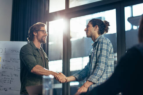 Young businessman shaking hands with male colleague after meeting in boardroom. Business handshake after successful meeting. - JLPSF22759