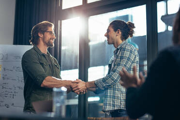 Zwei Geschäftsleute schütteln sich nach einem erfolgreichen Treffen die Hände. Ein Geschäftsmann beglückwünscht und würdigt die Leistung eines Kollegen im Besprechungsraum. - JLPSF22760