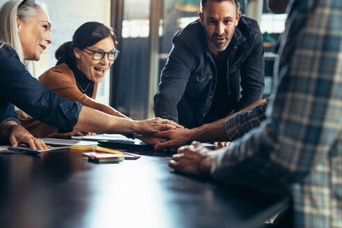 Eine Gruppe von Geschäftsleuten, die ihre Hände auf dem Tisch stapeln. Ein positives Geschäftsteam, das seine Hände übereinander legt, um Einigkeit und Teamwork zu zeigen. - JLPSF22764